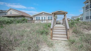A wooden staircase leading to a beach house with a covered porch and a view of other houses. - Rhoney R&R: Oceanfront Home With Two Living Rooms (Oak Island)