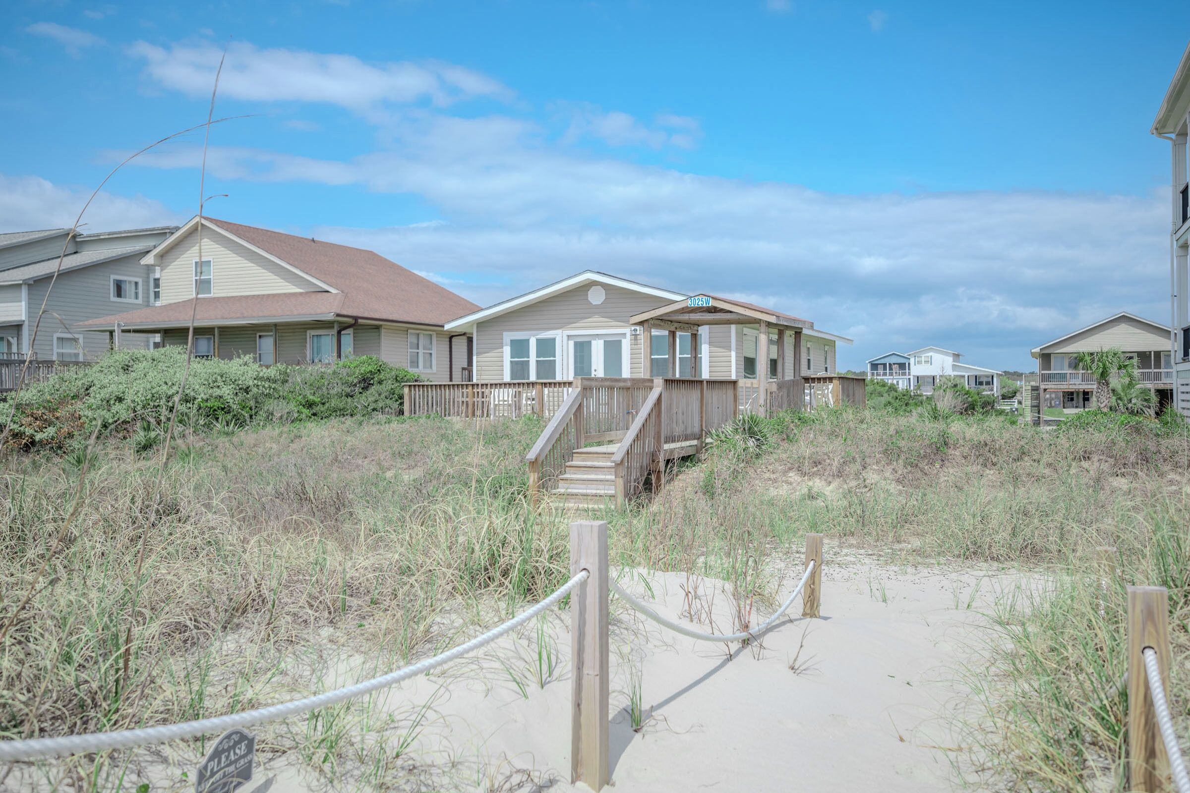A beachfront property with a wooden deck, a staircase leading to a covered porch, and a sandy path.