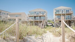 A beachfront property with multiple-story buildings featuring balconies and a sandy path leading to the entrance. - Salt & Light: Spacious, Custom-built, Oceanfront Home Close to Splash Pad, Park (Oak Island)