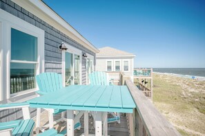 Une terrasse en bois avec une table et des chaises, donnant sur une plage et l’océan.
