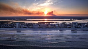 Un paisaje urbano costero con atardecer sobre el agua, que presenta rascacielos y una playa.
