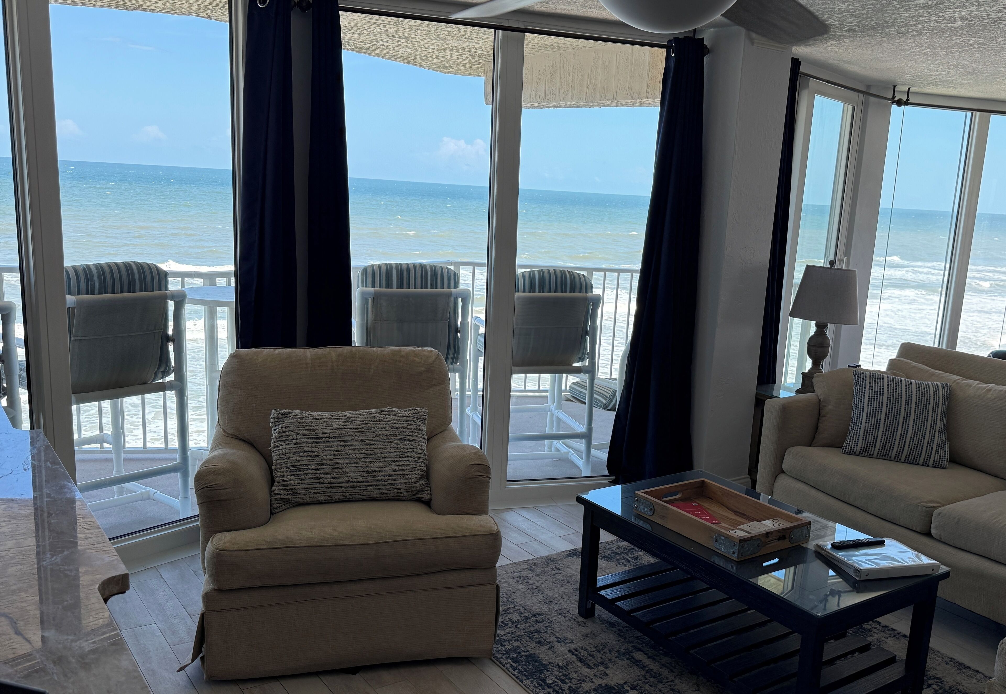 Sala de estar com vista para o oceano, um sofá, uma poltrona e uma mesa de centro.