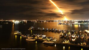 Un puerto deportivo de noche con barcos amarrados y un estela visible en el cielo.