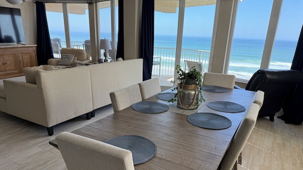 Un comedor con una mesa de madera, sillas tapizadas en beige y vista al océano.
