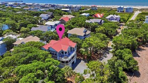 Vista aérea de una zona residencial costera con casas, una playa y un muelle al fondo.