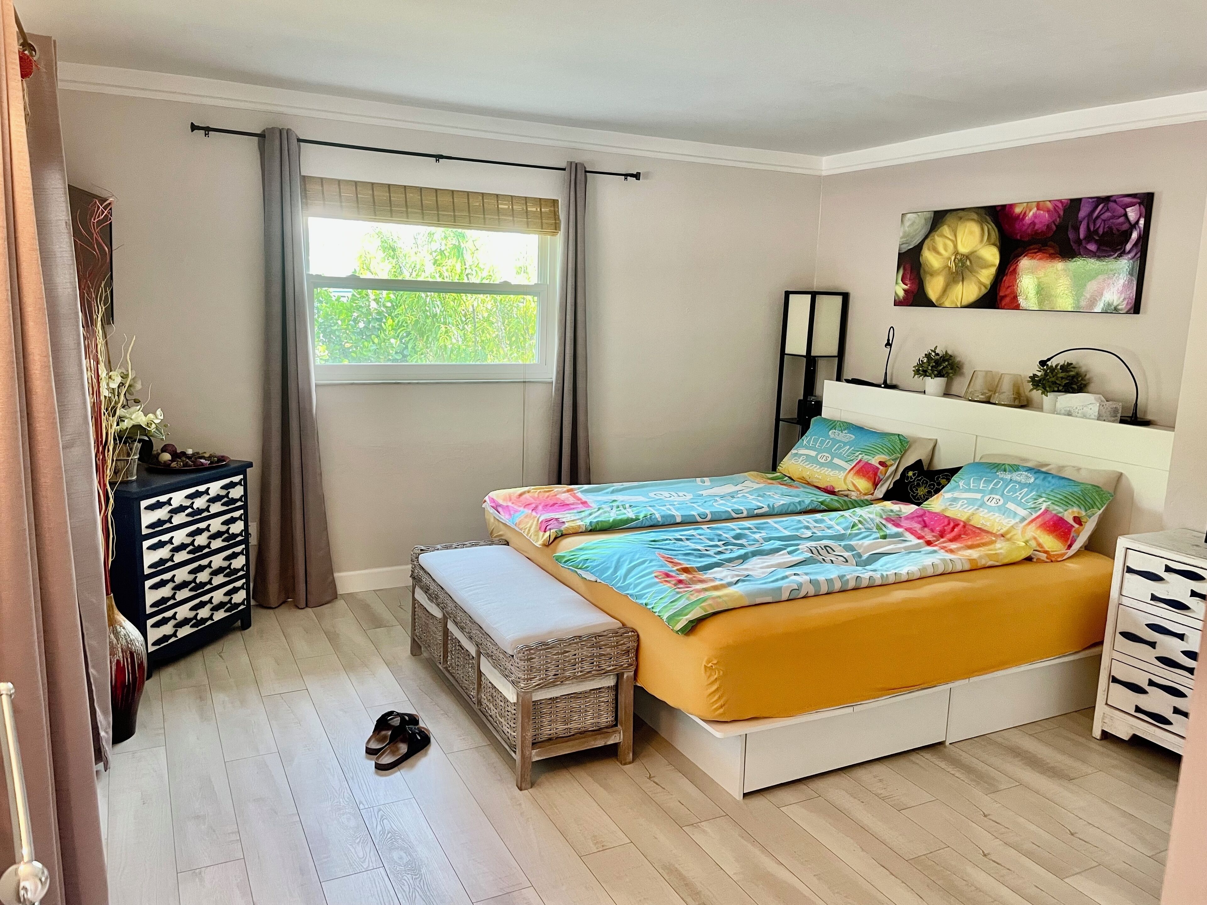 A bedroom with a bed, a bedside table, a window, and a wall-mounted shelf.