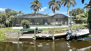 A house with a screened porch, a pool, and a boat docked by the water. - Vacation Home 6 minutes to the beach, heated pool, free canoe, free wifi  (Bonita Springs)