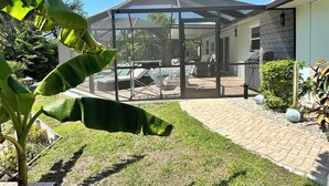 A covered patio area with a glass enclosure, outdoor furniture, and a cactus plant. - Vacation Home 6 minutes to the beach, heated pool, free canoe, free wifi  (Bonita Springs)
