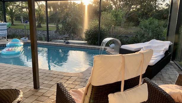 A poolside area with lounge chairs, a water feature, and a view of the surrounding garden. - Vacation Home 6 minutes to the beach, heated pool, free canoe, free wifi  (Bonita Springs)