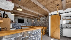 Una cocina rústica con pared de piedra, vigas de madera en el techo y una barra de bar de madera.
