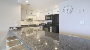 Una cocina moderna con encimeras de granito, armarios blancos, un refrigerador negro y un microondas.