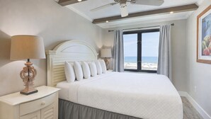 Un dormitorio con cama, mesita de noche, lámpara, ventilador de techo y vista al mar.