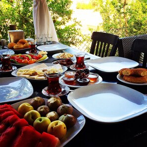 A table set outdoors with various dishes, including fruits and bread, and a pitcher of red beverage. - Kamelya Butik Otel (Bozcaada)