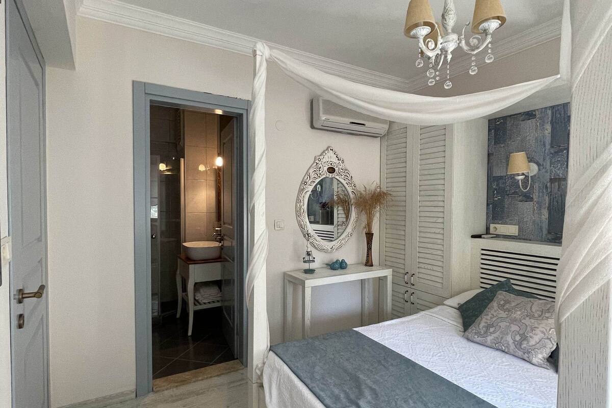 A bedroom with a bed, bedside table, mirror, and a chandelier.