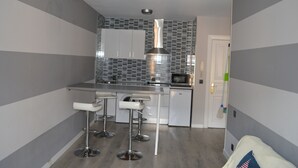 A compact kitchen with a microwave, stainless steel appliances, and a tiled backsplash. There are three white bar stools and a white door leading to another room. - Hotel Los Robles (Cangas de Onis)