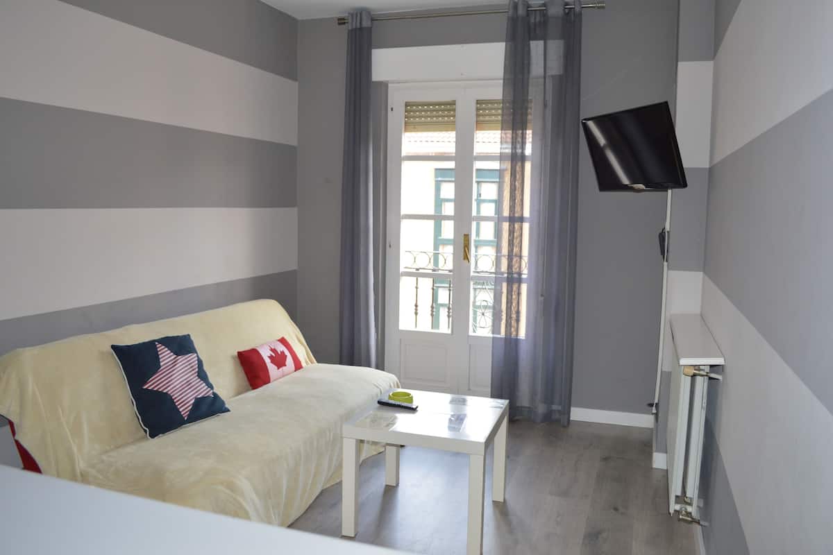 A room with a bed, a small table, a TV, and a window with curtains.