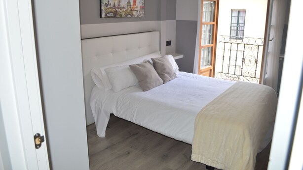 A bedroom with a bed, pillows, a headboard, a painting on the wall, and a balcony with a railing. - Hotel Los Robles (Cangas de Onis)