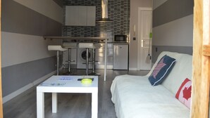 A compact living space with a kitchenette, a dining area, and a sofa with pillows. - Hotel Los Robles (Cangas de Onis)