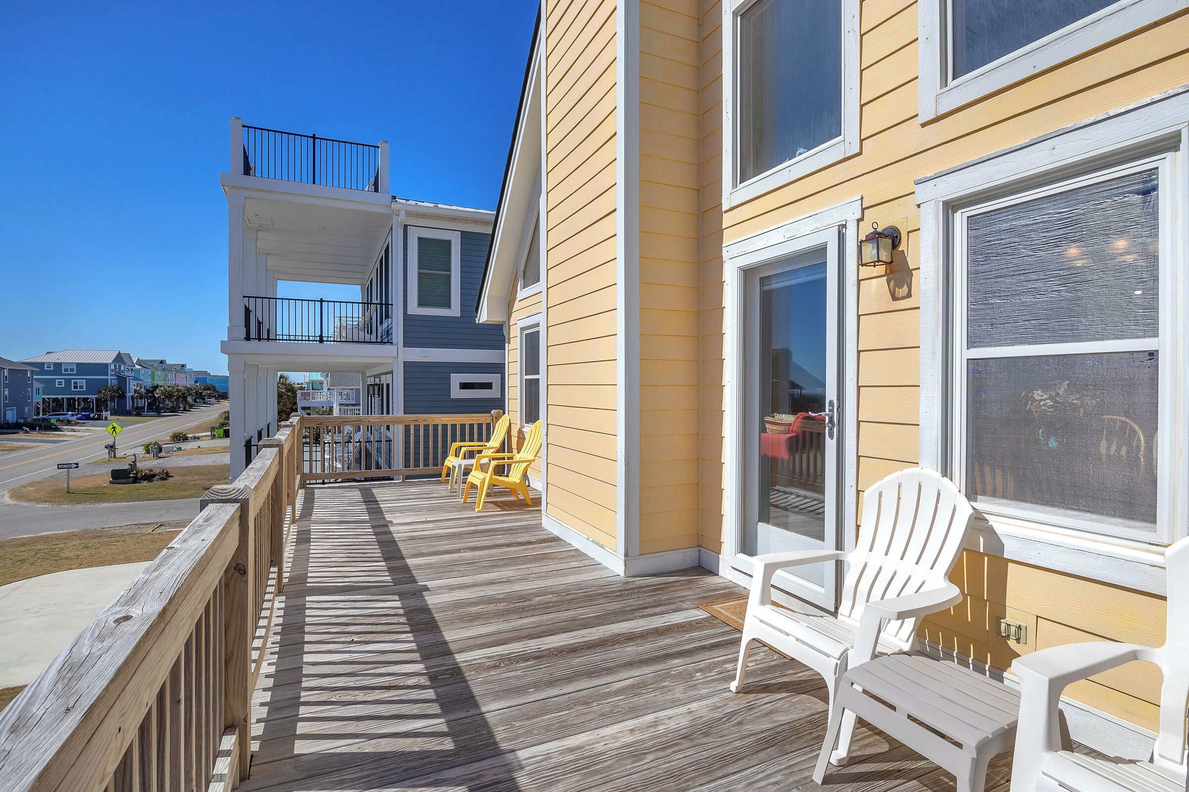 Une terrasse en bois avec des chaises, une rambarde et une vue sur la rue.