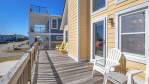 A wooden deck with chairs, a railing, and a view of a street. - Sandtrap: Oceanview House on West Beach with Easy Beach Access. (Oak Island)