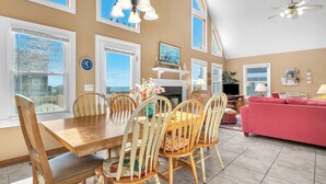 A dining area with a wooden table and chairs, a fireplace, and a view of the outdoors. - Sandtrap: Oceanview House on West Beach with Easy Beach Access. (Oak Island)