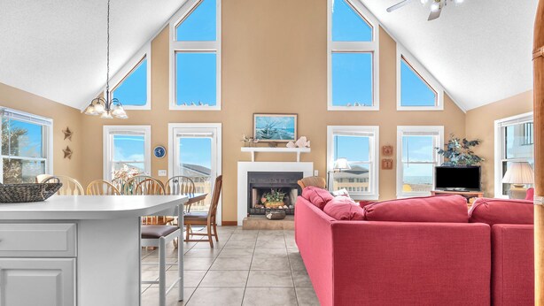 A spacious living area with a fireplace, a red sofa, and a dining area with a white table and chairs. - Sandtrap: Oceanview House on West Beach with Easy Beach Access. (Oak Island)