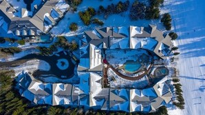 Vue aérienne d’un complexe hôtelier comprenant plusieurs bâtiments, une piscine centrale et des zones environnantes recouvertes de neige.