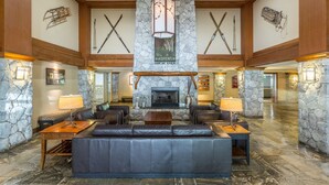 Un hall d’entrée spacieux avec une cheminée en pierre, des fauteuils en cuir et une décoration sur le thème du ski.