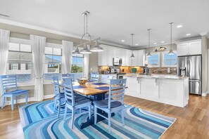 Une cuisine moderne avec des meubles blancs, un îlot central, des appareils en acier inoxydable et des chaises bleues disposées autour d’une table en bois.