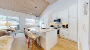 Een moderne keuken met witte kastjes, een centraal eiland en een zithoek met een bank en stoelen.