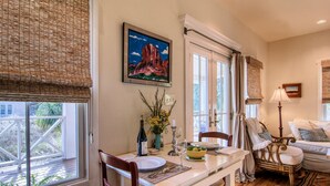 Un comedor con una mesa dispuesta para dos, un cuadro sobre la mesa y vistas al exterior a través de la ventana.