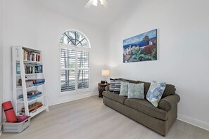 A living room with a white bookshelf, a green sofa, and a painting on the wall. - Relaxing Waterfront Home | Pool & Steps to Beach (Marco Island)