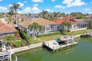 A residential area with a dock, a greenhouse, and houses with red roofs. - Relaxing Waterfront Home | Pool & Steps to Beach (Marco Island)