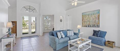A spacious living room with a light blue sofa, a white coffee table, and a large painting on the wall.