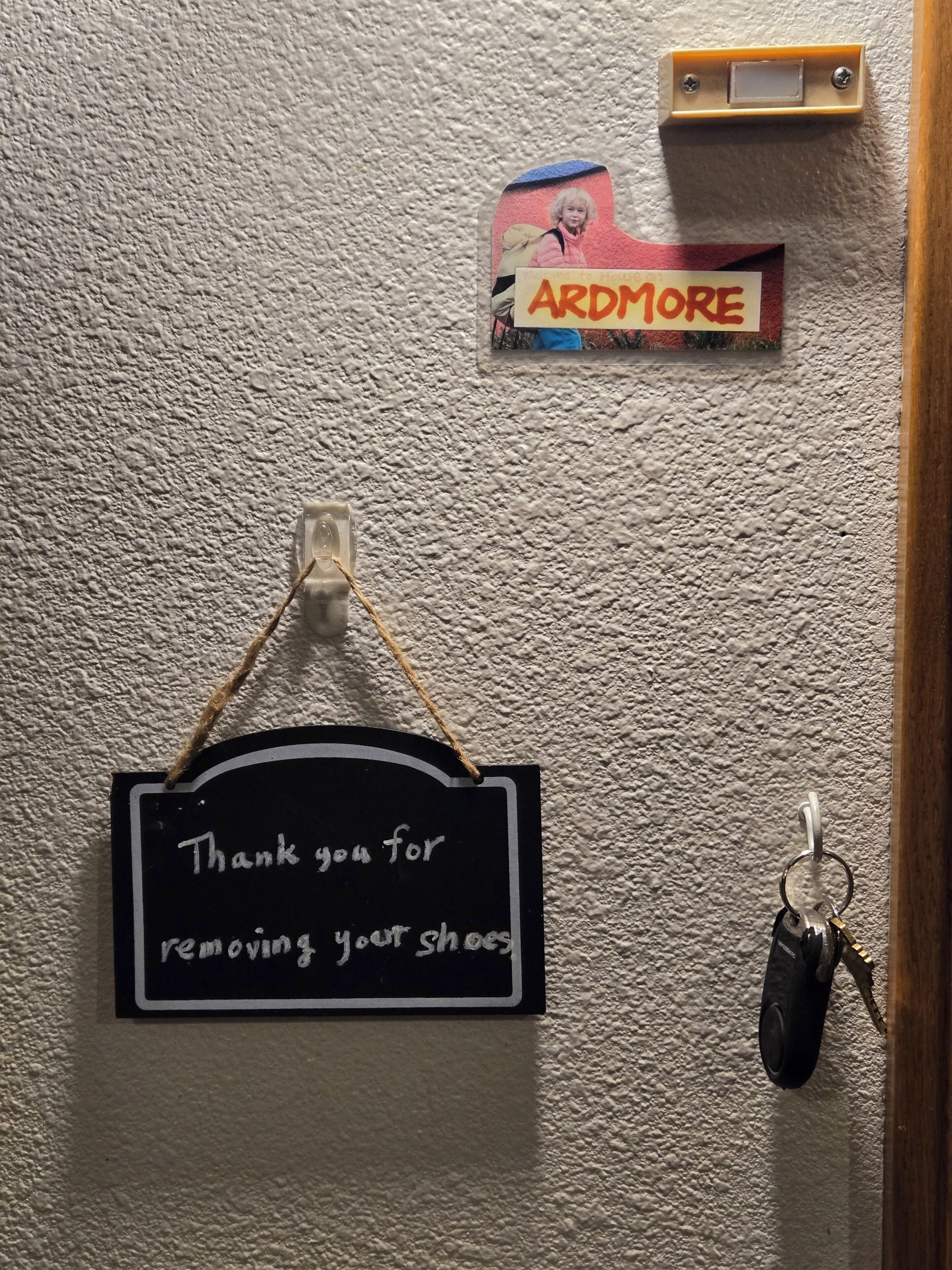 Una pared con un cartel que dice 'Gracias por quitarse los zapatos', un llavero y un termostato.