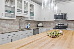 Una cocina con armarios blancos, encimera de granito, microondas de acero inoxidable y una isla de madera con una planta.