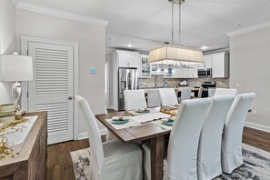 A dining area with a wooden table, white chairs, and a hanging light fixture.