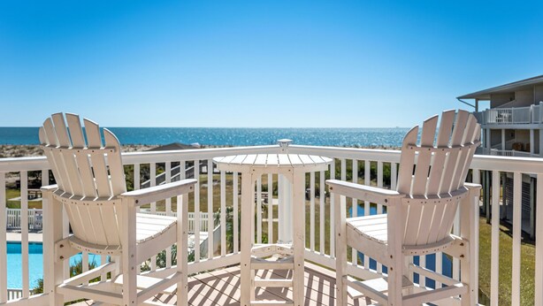 Une terrasse en bois peinte en blanc, avec deux fauteuils Adirondack, donnant sur une piscine et offrant une vue sur l’océan.