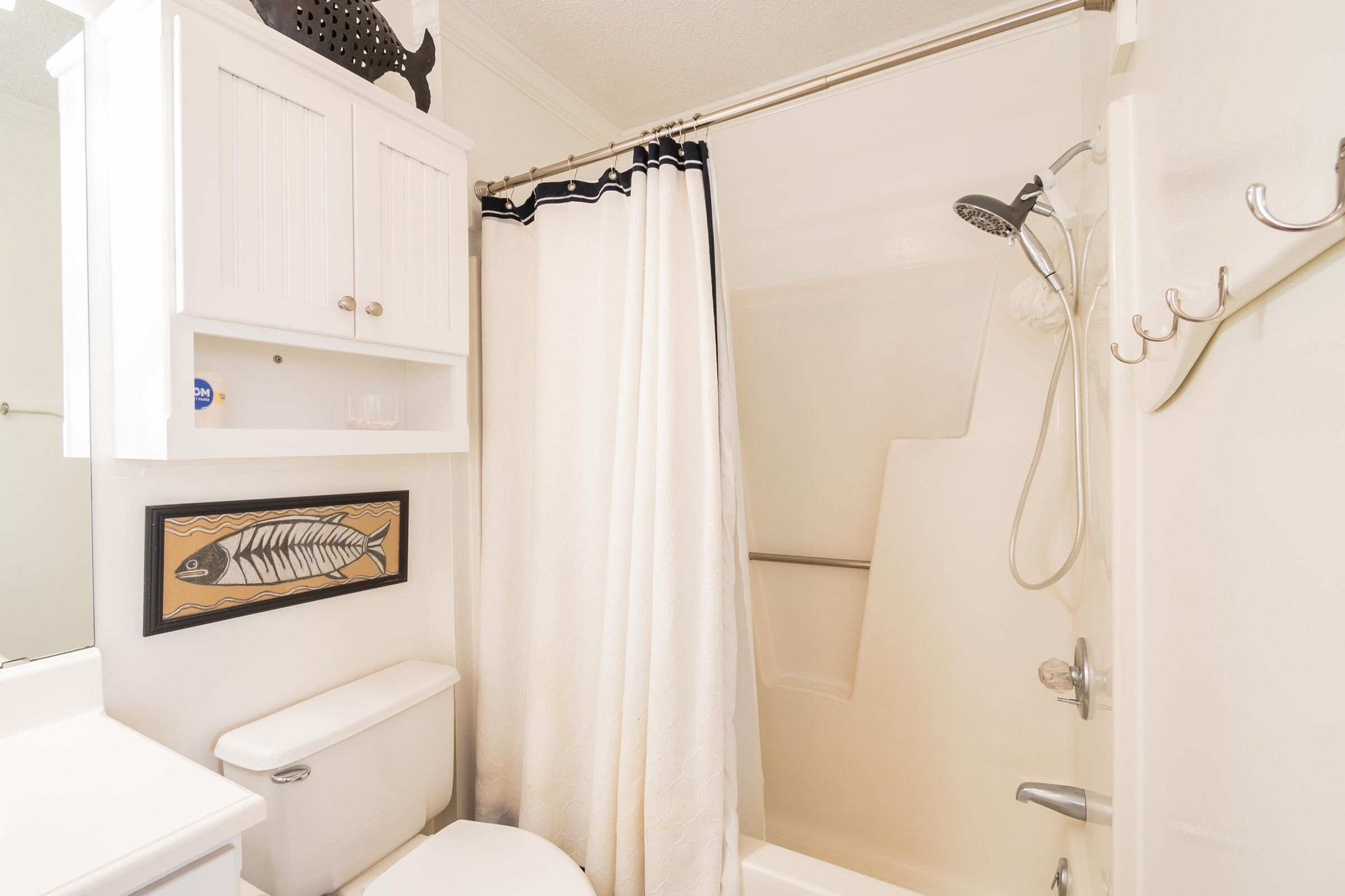 Une salle de bain comprenant des toilettes, une douche et un meuble décoré avec un motif de poisson.