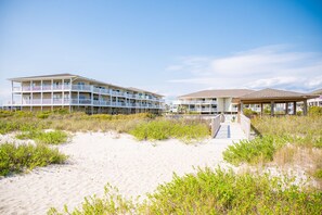 Ett hotell vid stranden med flera balkonger, en sandstrand i förgrunden och en klar himmel.