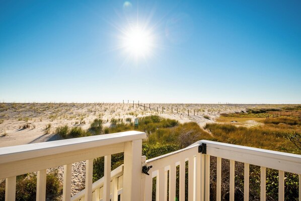 A beach view from a wooden deck with a clear sky and sun shining.