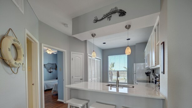 A modern kitchen with a white island, bar stools, and a view of a bedroom. - Large Updated BEAUTIFUL 2BR, 2 BATH Condo! Walk to Beach, Pool & More! (Corpus Christi)