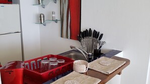 Kompakti keittiö, jossa on sisäänrakennettu mikroaaltouuni, punainen roskakori, punainen muovikori ja puinen penkki.