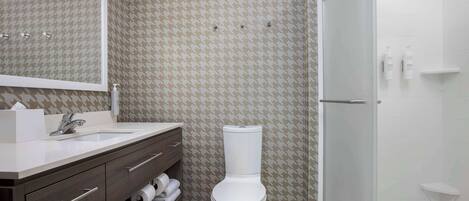 A bathroom with a houndstooth patterned wall, a white toilet, a sink with a mirror, and a glass shower enclosure.