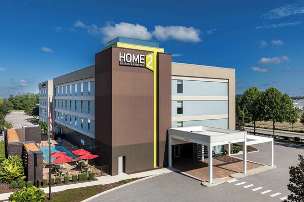 A modern hotel with a sign reading "HOME 2 Suites by Hilton" and a covered outdoor area with umbrellas. - Home2 Suites by Hilton Clermont (Clermont)
