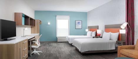 A hotel room with a desk, two beds, a TV, and a window with curtains.
