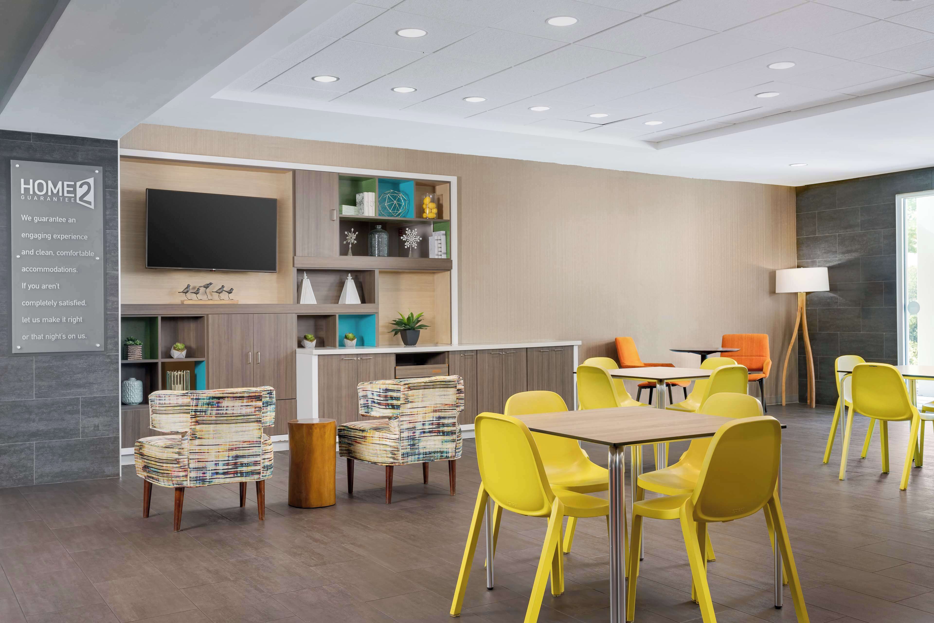 Un espace repas moderne avec des chaises jaunes, une table en bois et un téléviseur fixé au mur.