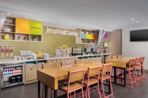 A modern cafe with a wooden counter, multiple tables, and chairs. - Home2 Suites by Hilton Clermont (Clermont)
