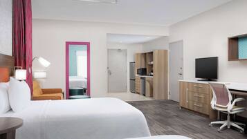 Een hotelkamer met twee bedden, een bureau, een stoel, een televisie, een bureaulamp en een kitchenette.