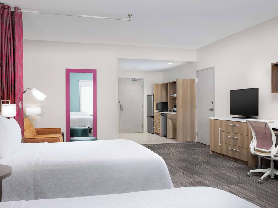 Een hotelkamer met twee bedden, een bureau, een stoel, een televisie, een bureaulamp en een kitchenette.